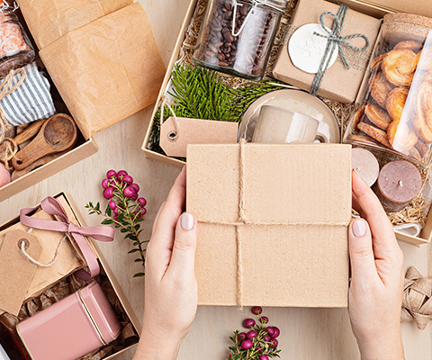 hands holding a brown gift box surrounded by various wrapped gifts and seasonal decorations perfect for gifting and special occasions